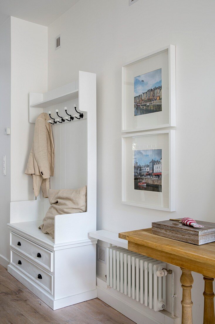 Cushions and coat pegs on white cloakroom cabinet next to framed photos