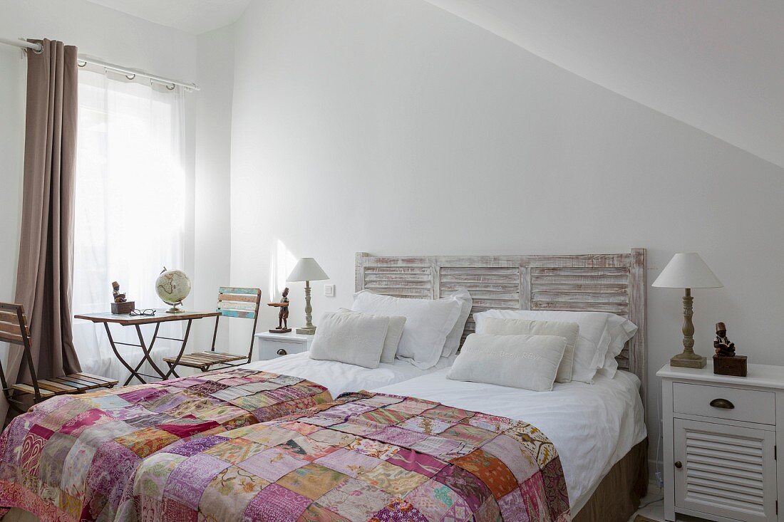 Doppelbett mit Betthaupt, Patchworkdecken und Vintage Gartentisch mit Klappstühlen vor Fenster