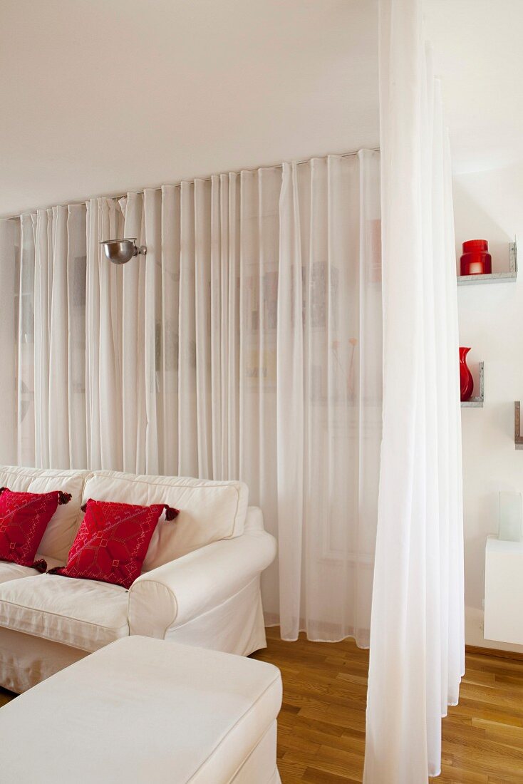 White curtain partition around loose-covered sofa and pouffe