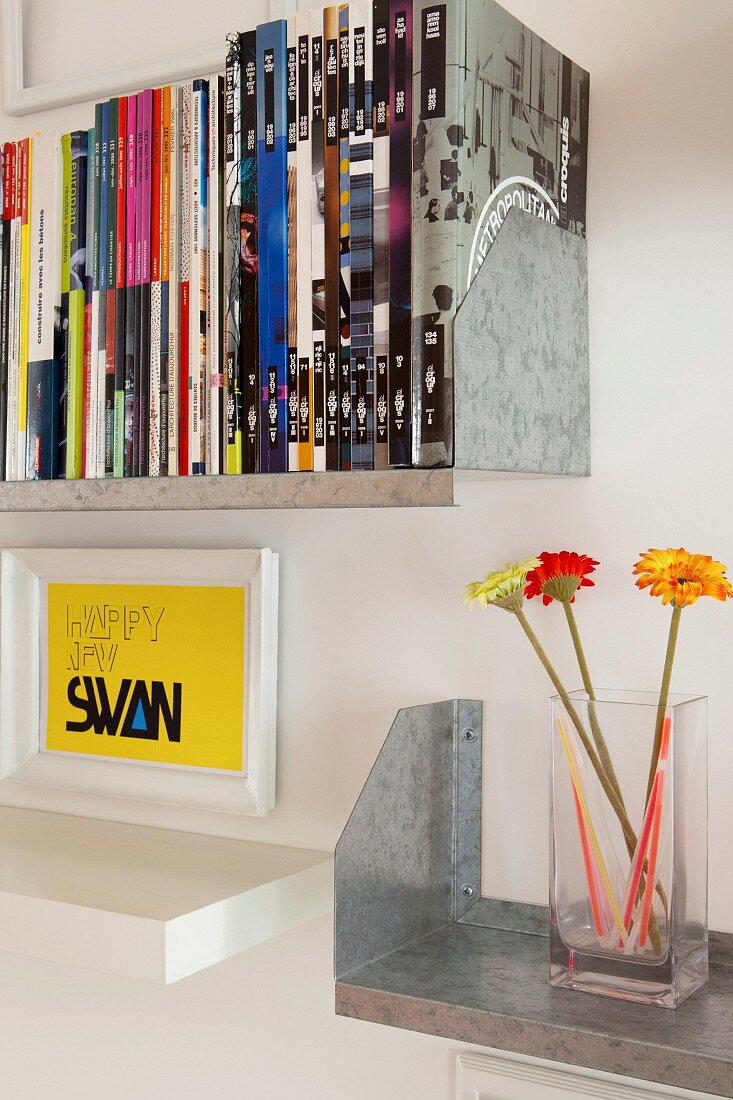 Framed lettering above white floating shelf and books and glass vase on metal shelves
