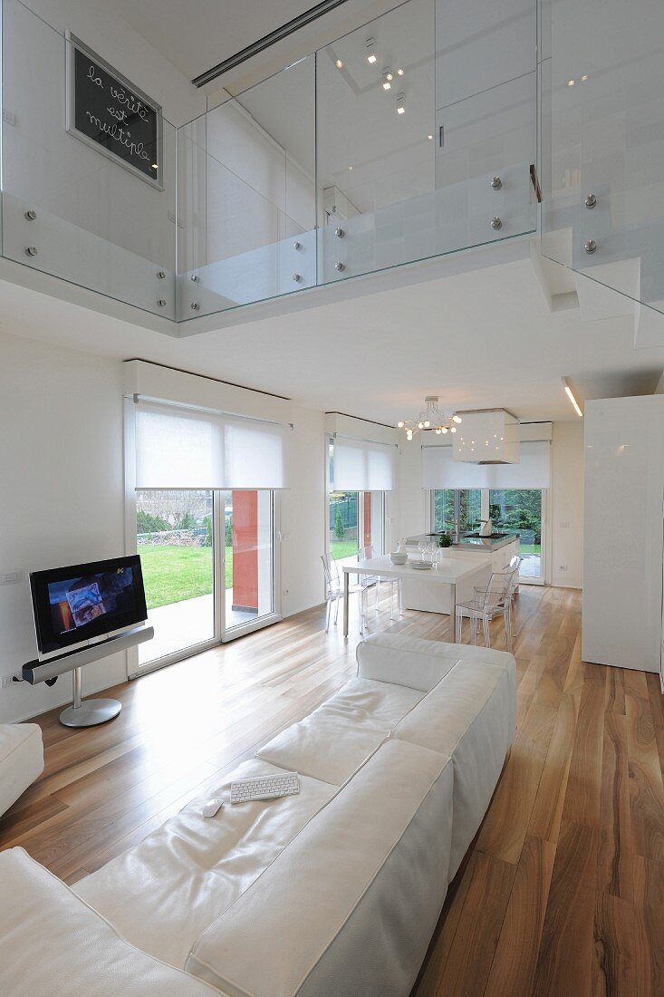 White leather couch, exotic-wood parquet floor and glass balustrade on upper storey in elegant, open-plan interior