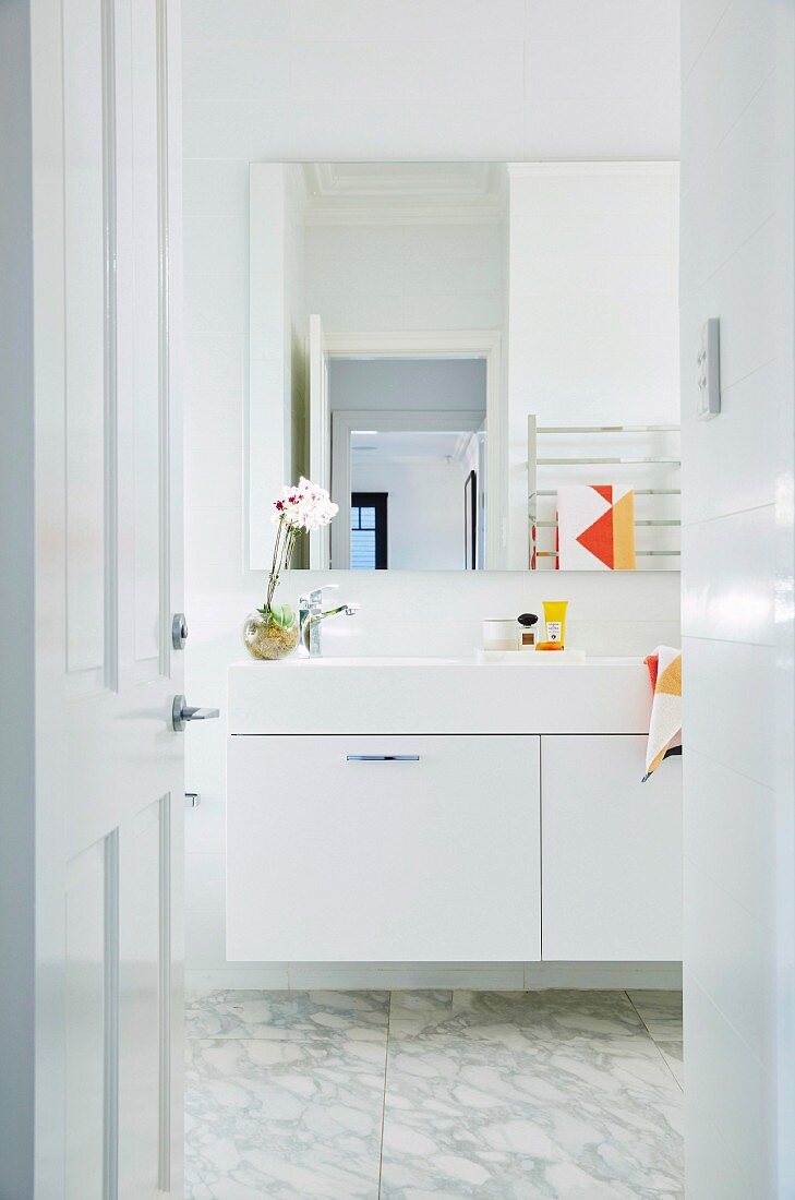 View through open door into the white bathroom with marble floor