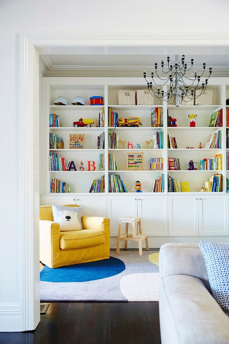 Gelber Sessel vor Regalwand mit bunten Büchern und Spielzeug