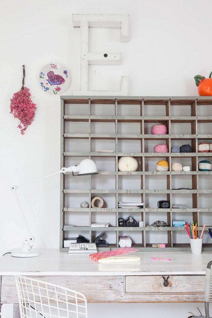 Balls of yarn and office utensils on wooden shelves above vintage desk