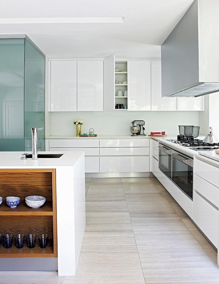 White glossy kitchen cupboards, island counter and stone-tiled floor