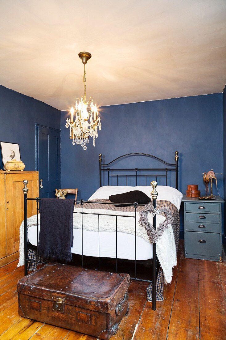 Metal bed in small bedroom with blue walls and old wooden floor