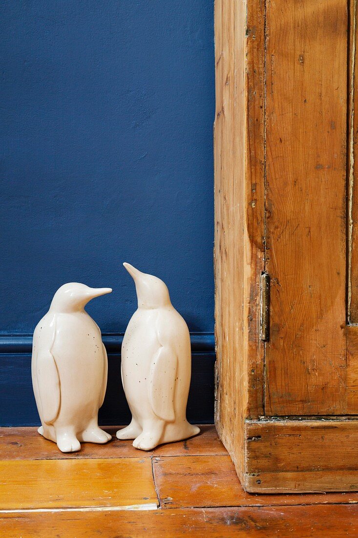 Two white penguin figurines on wooden floor against blue wall