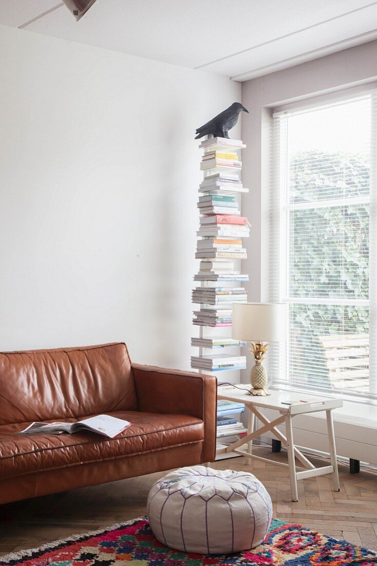 Leseecke mit Sitzpouf und Ledercouch neben Bücherständer und Tabletttisch mit Tischleuchte