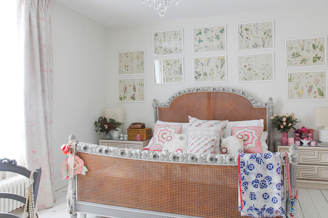 Double bed with wicker headboard and foot below framed botanical illustrations on white bedroom wall