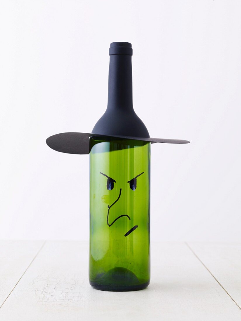Flasche dekoriert mit Hutkrempe aus Papier und aufgemaltem grimmigen Gesicht