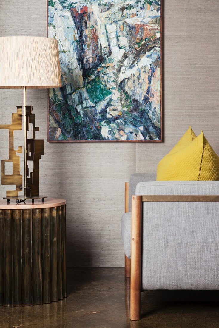 Grauer Sessel und Tischlampe vor Wand mit Gemälde