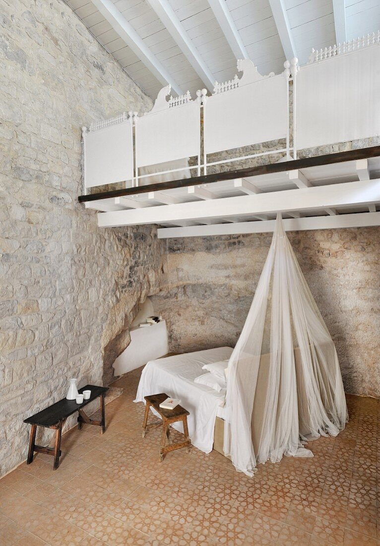 Restored bedroom with stone wall, white wooden gallery and patterned tiled floor
