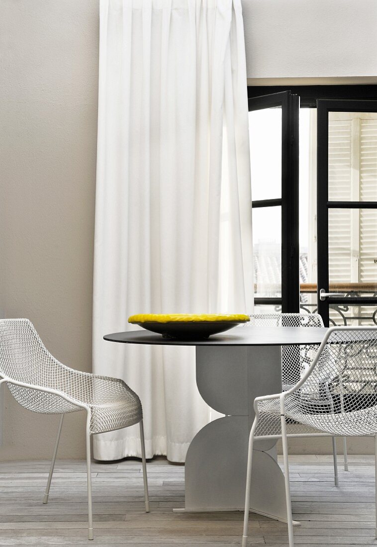 Designertisch mit Metallstühlen vor Fenstervorhang auf der Dachterrasse
