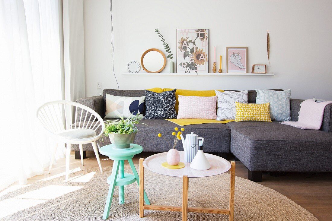 Hocker und Tablettisch vor grauem Sofa mit pastellfarbenen Kissen