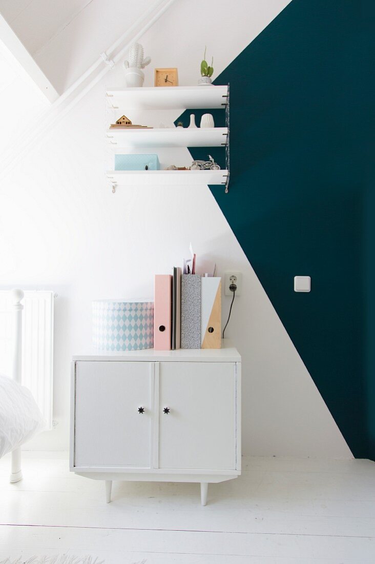 Small white retro cabinet below shelves mounted on two-tone wall