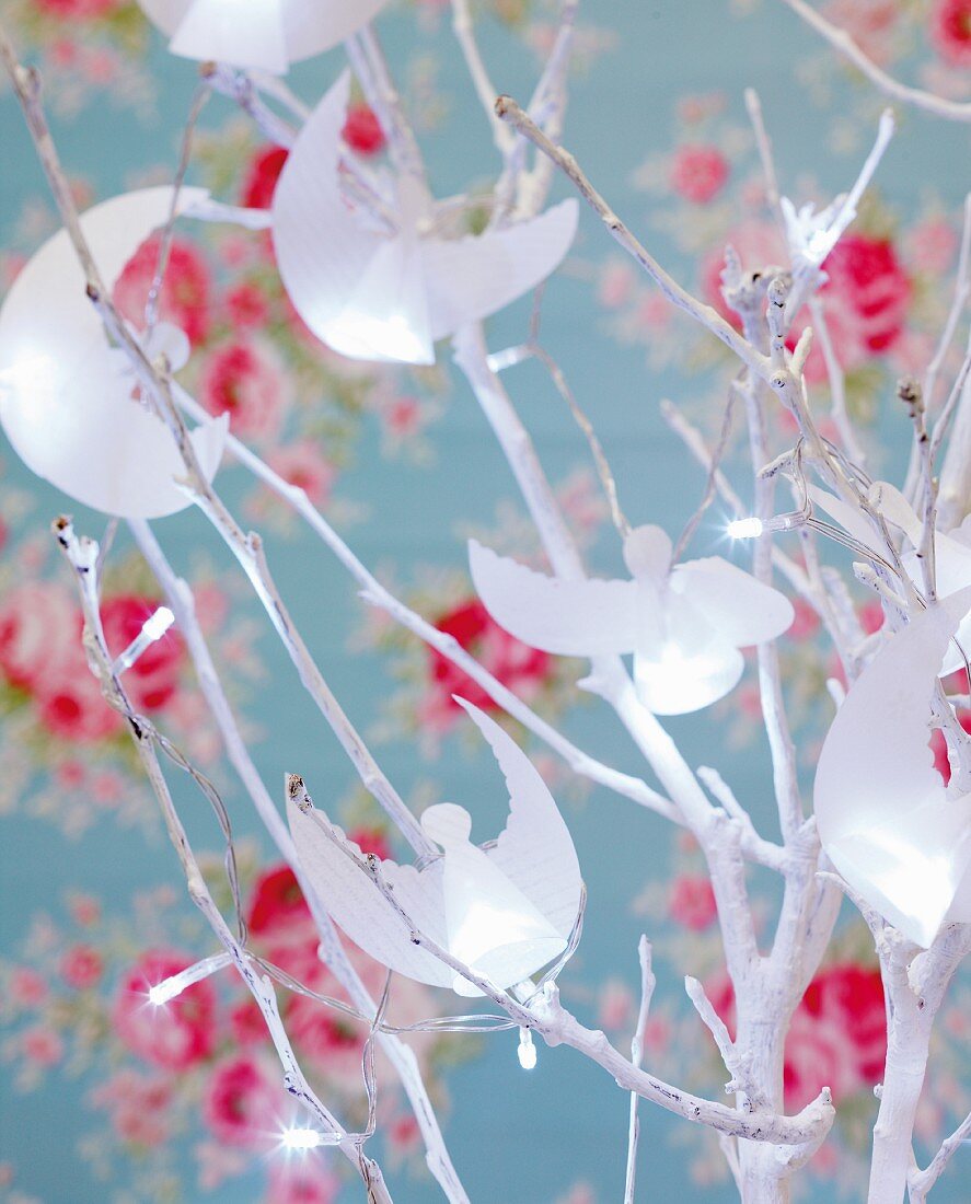 Papier-Engeln an weiß besprühtem Zweig mit Lichterkette