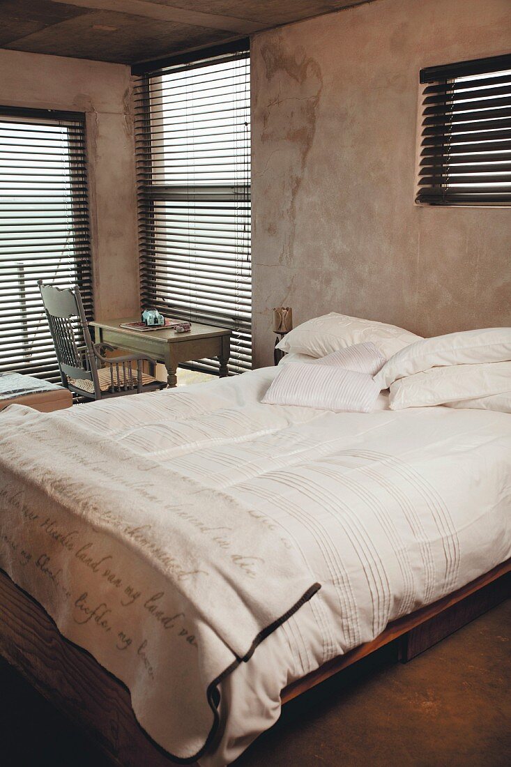 Abgedunkeltes Schlafzimmer mit Doppelbett, türkisfarbenem Schreibtisch und Armlehnstuhl