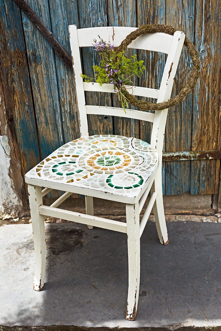 Kranz mit Blumen hängt an Stuhl mit Mosaik auf der Sitzfläche