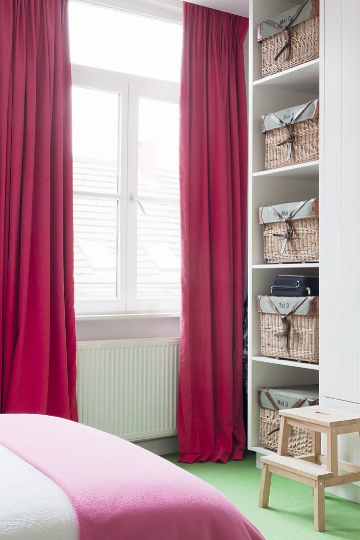Schlafzimmer mit roten Vorhängen und Aufbewahrungskörben in weißem Schrank