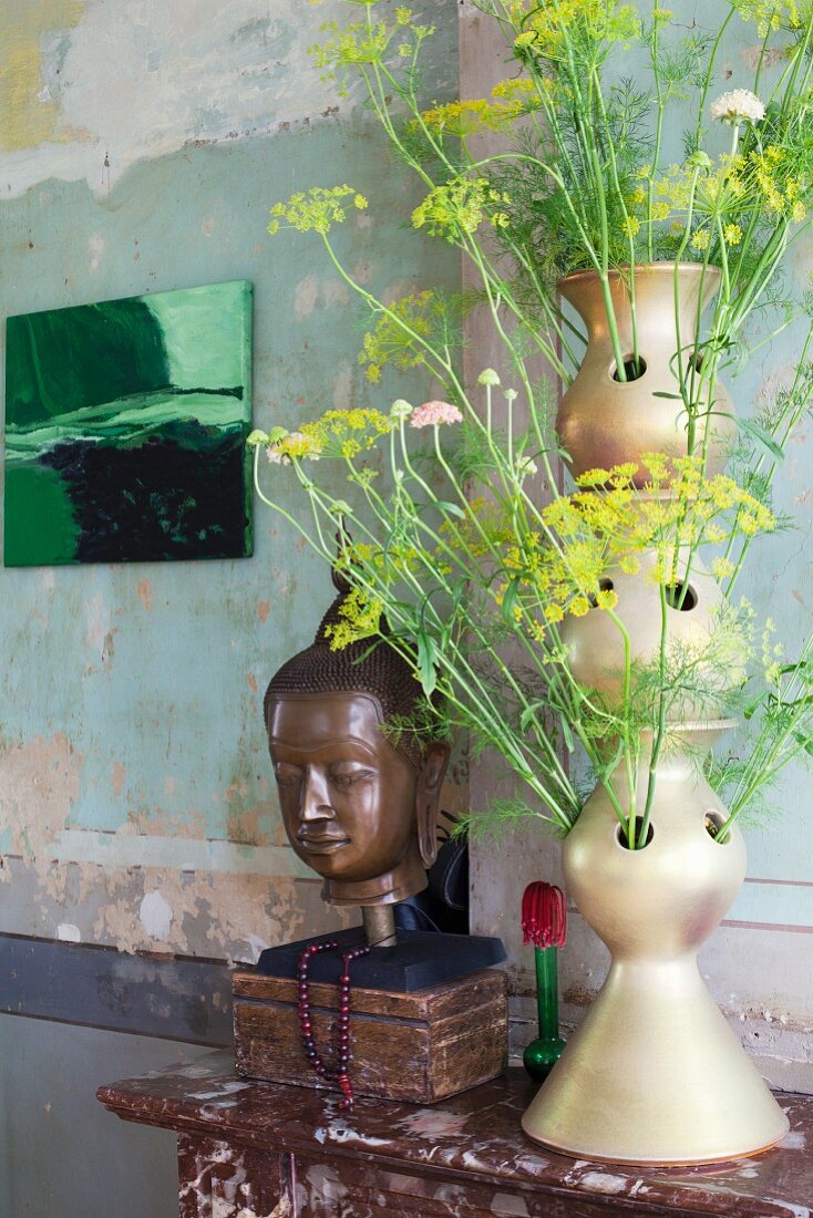 Künstlerische Vasenform mit Blütenstängel neben Buddhakopf in Vintage Ambiente