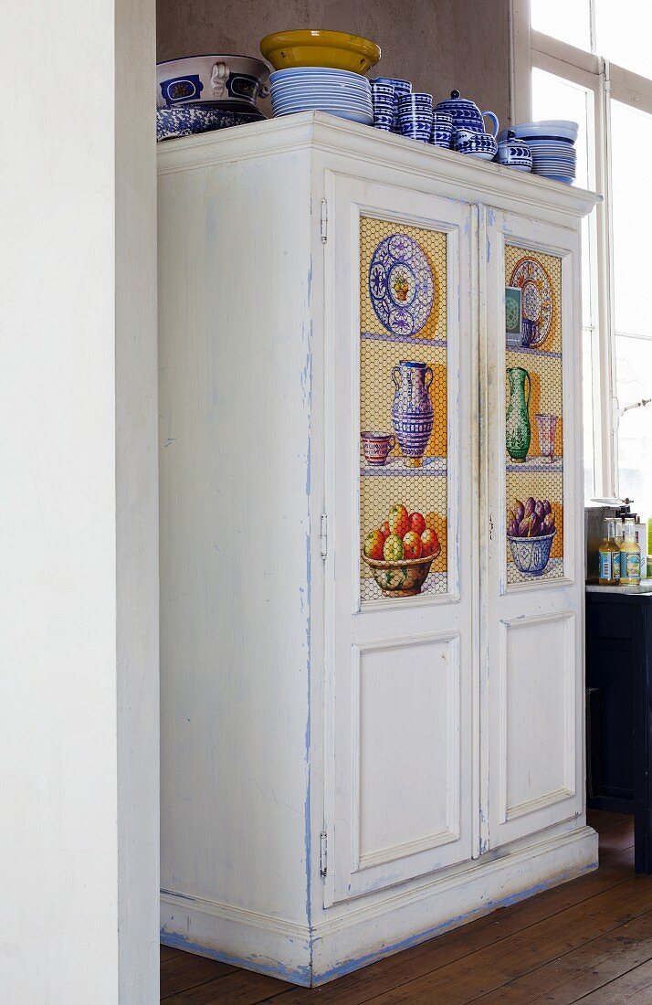 White vintage cupboard with painted panels and blue and white crockery on top