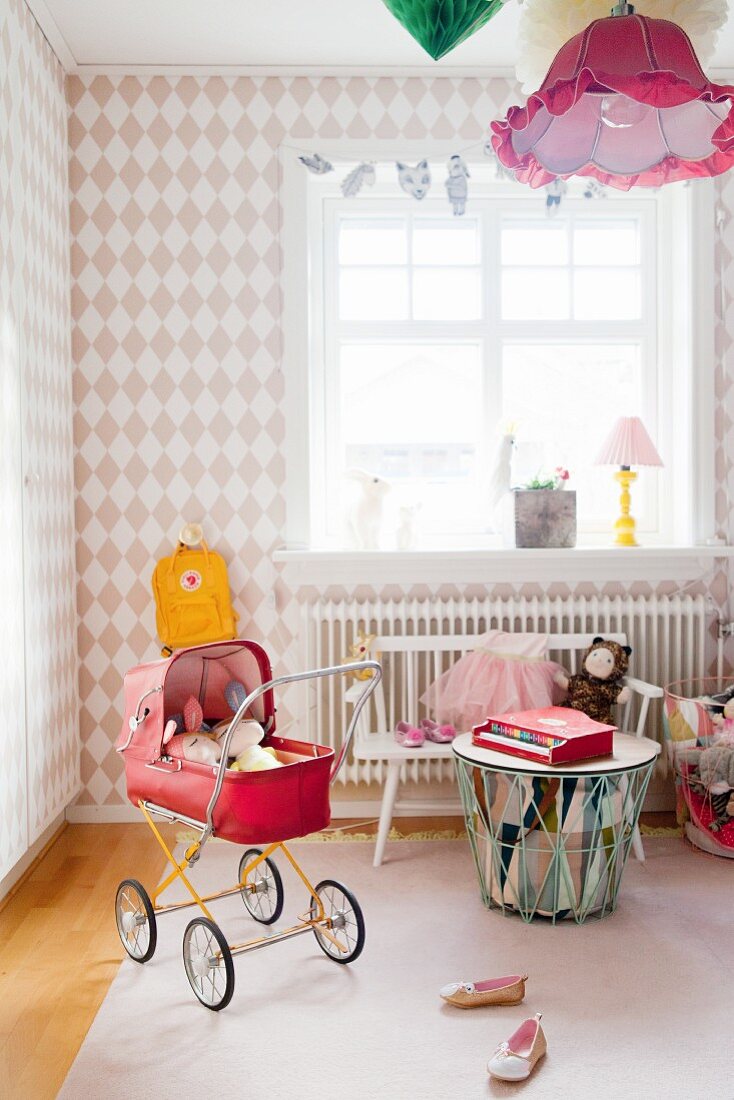 Diamond-patterned wallpaper and red retro dolls' pram in girl's bedroom