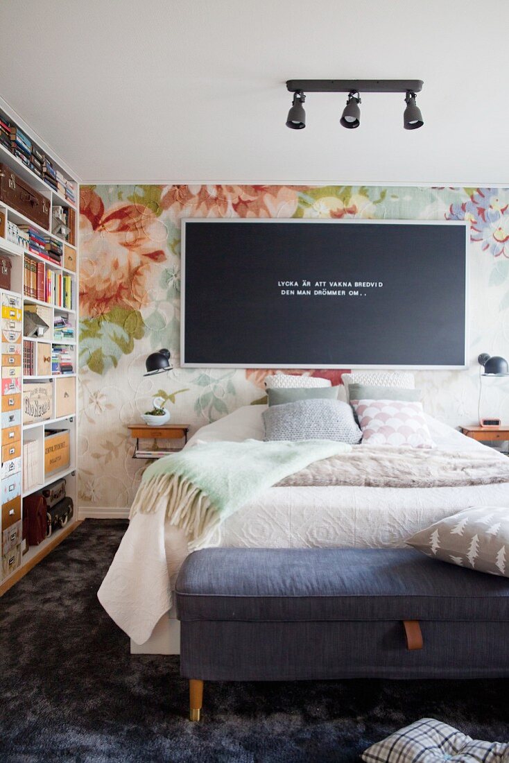 Black letter board with white peg letters on floral textile wallpaper and retro shelving in bedroom