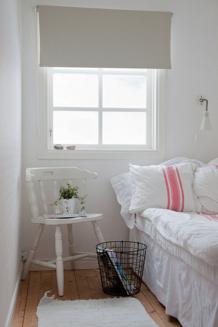 White wooden chair and metal basket below window and next to bed