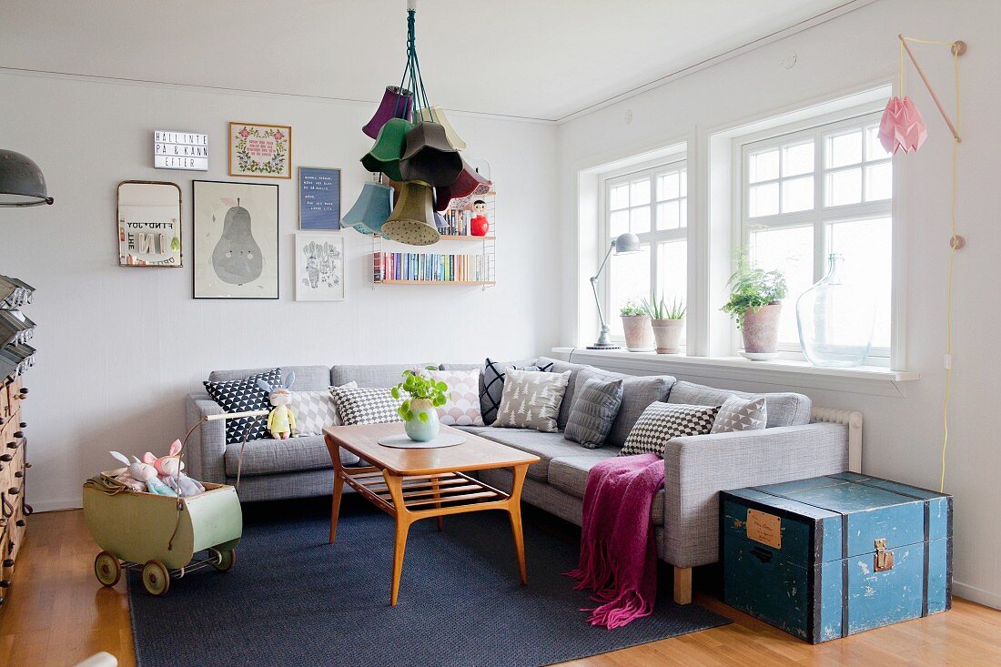 Gemütliches Wohnzimmer mit grauer Couch, Kissensammlung, Vintage Puppenwagen und Retroflair