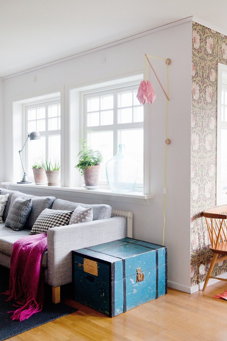 Helle Wohnzimmerecke mit blauer Holztruhe, Wandleuchte und Blumentapete