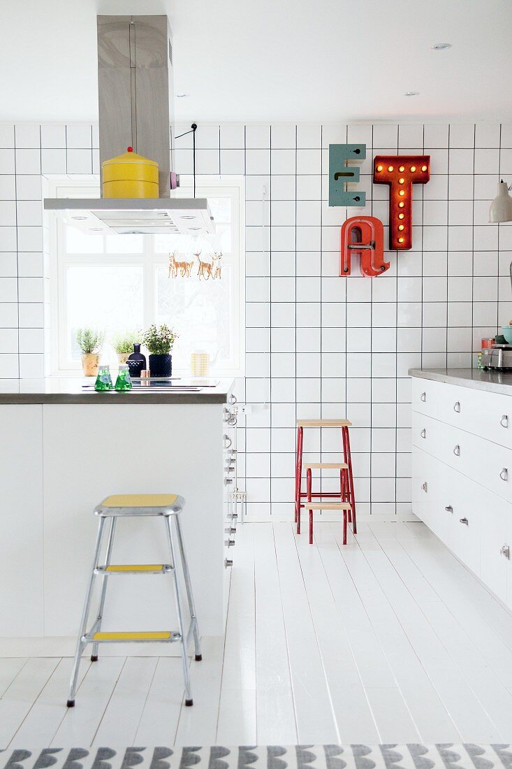 weiße Einbauküche mit bunten Farbakzenten, Kücheninsel und Leuchtbuchstaben als Wanddekoration