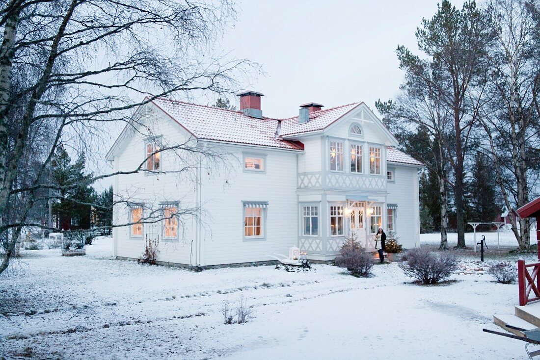 White Swedish house with illuminated windows in winter landscape