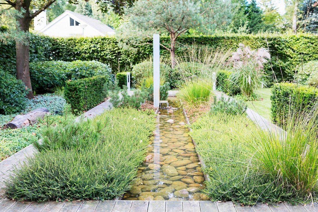 Gartengestaltung mit geradem Wasserlauf, Büschen, Ziergras und Laubhecken