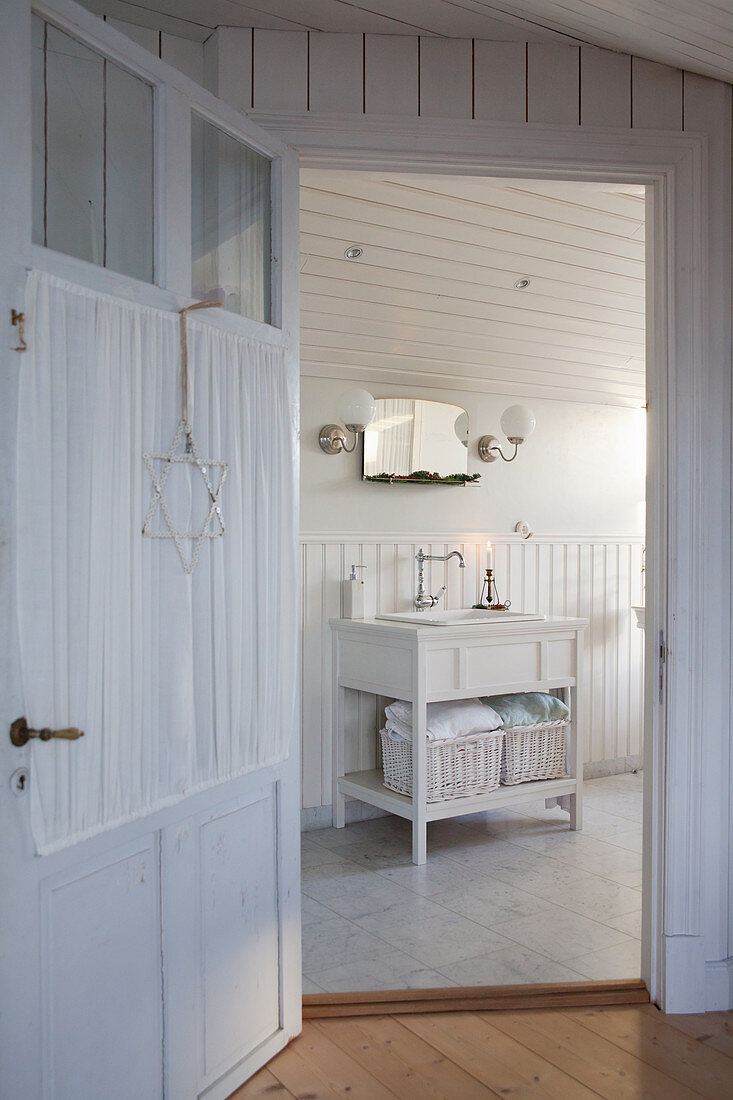 Blick durch Sprossentür mit Gardine ins weiße Bad mit Holzverkleidung