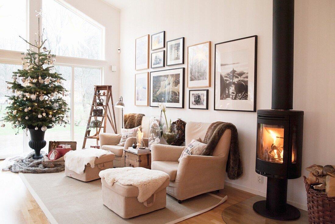 Schwedenofen mit Feuer in Wohnzimmer mit hellem Polstergarnitur und geschmücktem Weihnachtsbaum