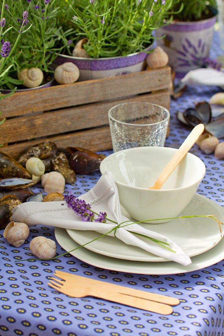 Gedeckter Gartentisch mit lila Tischtuch und weißem Geschirr, Tischdekoration mit Muschelschalen und Schneckengehäuse