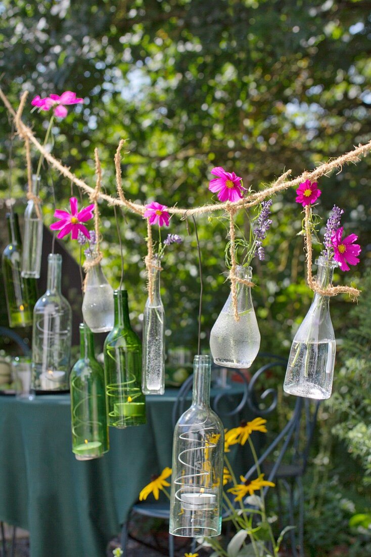 Glasflaschen mit pinkfarbenen Kosmeen und Teelichtern an rustikalem Seil aufgehängt