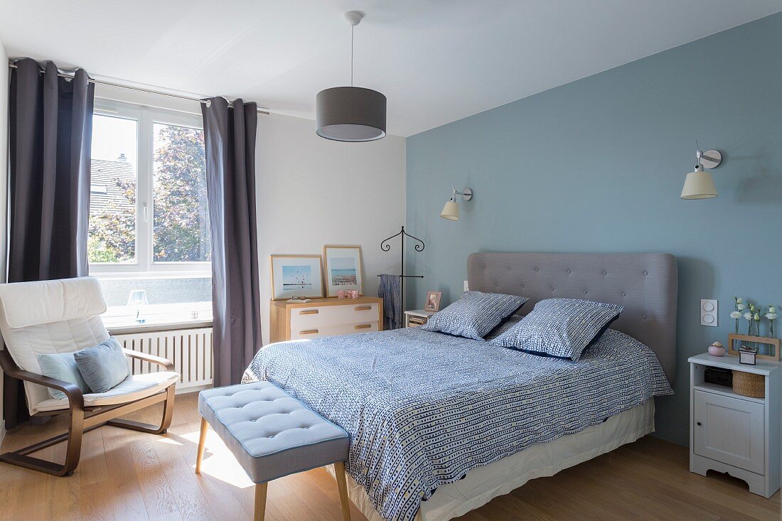 Schlafzimmer mit pastellblauer Wand und grau gepolstertem Betthaupt