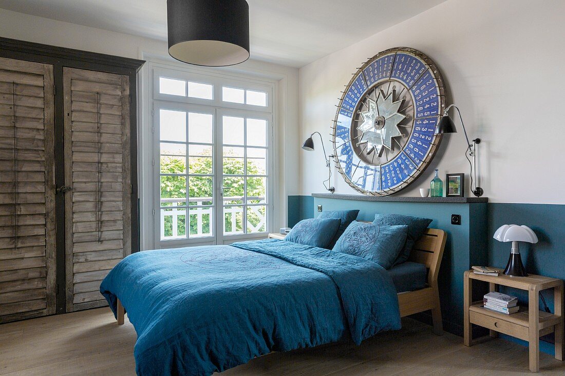 Schlafzimmer mit petrolfarbener Wandgestaltung und passender Bettwäsche, rundes Kunstobjekt als Wanddekoration