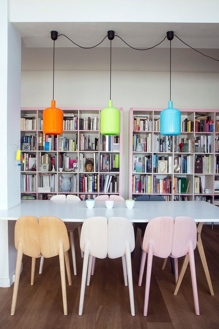 weiße Tischplatte und bunte Pendelleuchten vor rosafarbenem Bücherregal