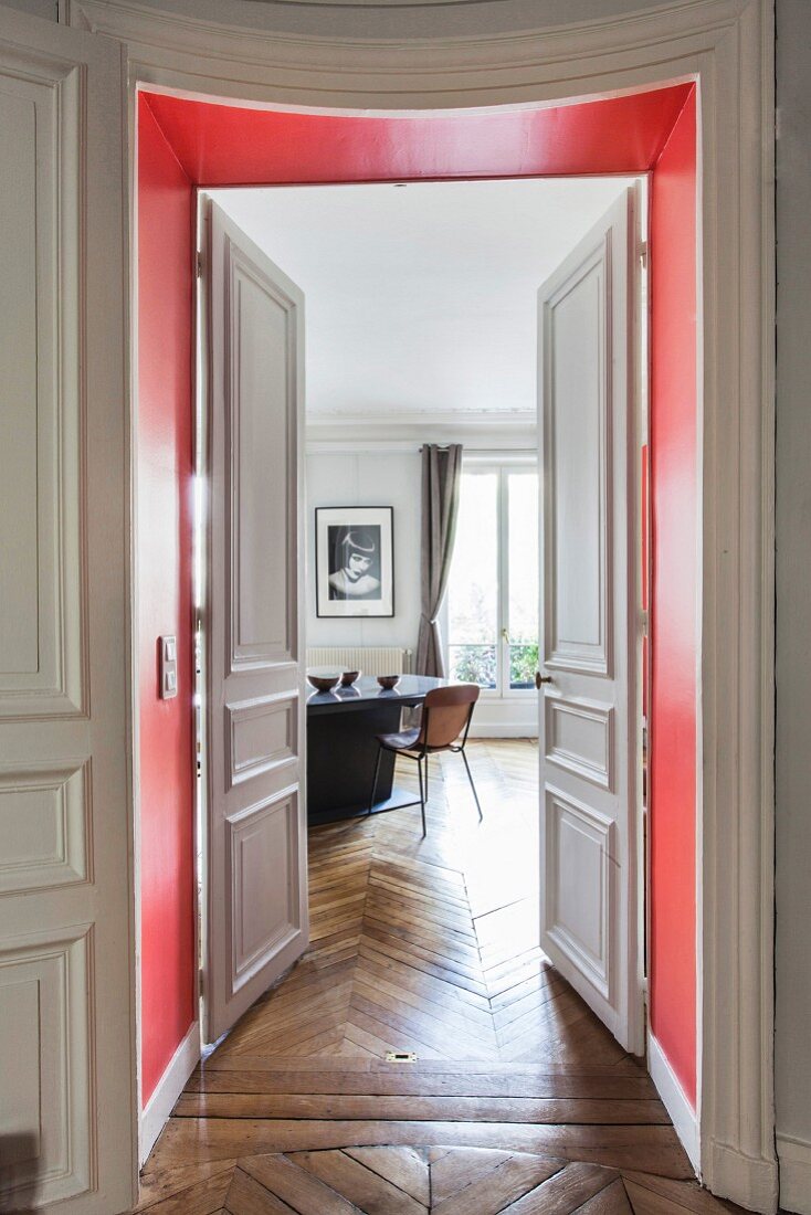 Blick durch rote Türlaibung und geöffnete Kassetten-Flügeltür auf Essbereich in Altbauwohnung