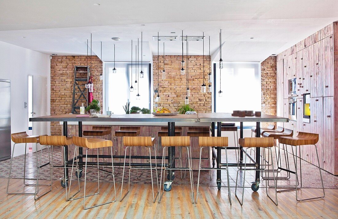 Designer bar stools at long dining table on castors in open-plan interior