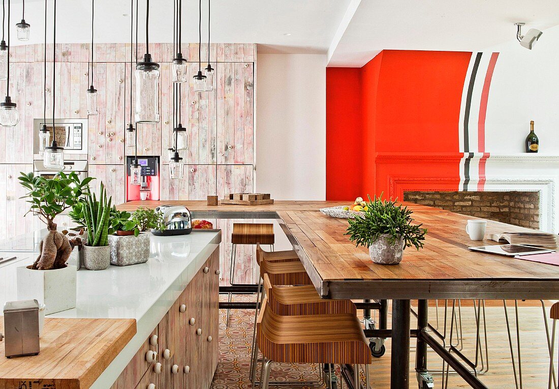 Kücheninsel mit weisser Arbeitsfläche, Pendelleuchten aus Gläsern und langer Esstisch mit Barhockern in offenem Wohnraum