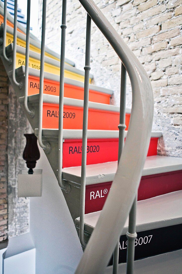 Winding staircase with risers in various RAL standard paint shades in staircase with exposed brick wall