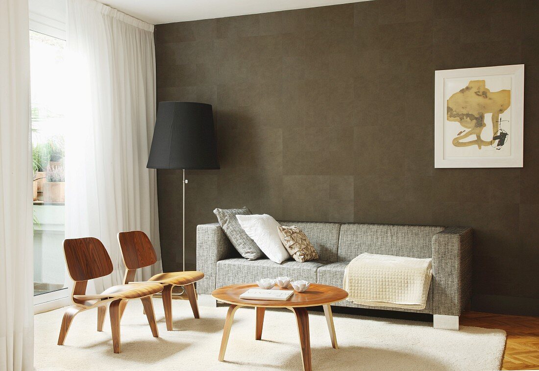Klassikerstuhl mit Coffeetable, Sofa und Stehleuchte vor brauner Wand im Wohnzimmer