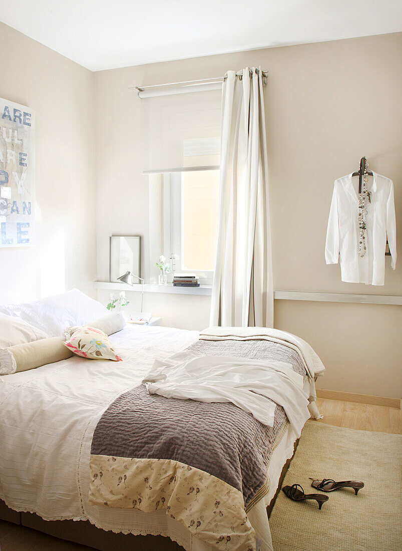 Double bed in bright bedroom with blouse hung on wall