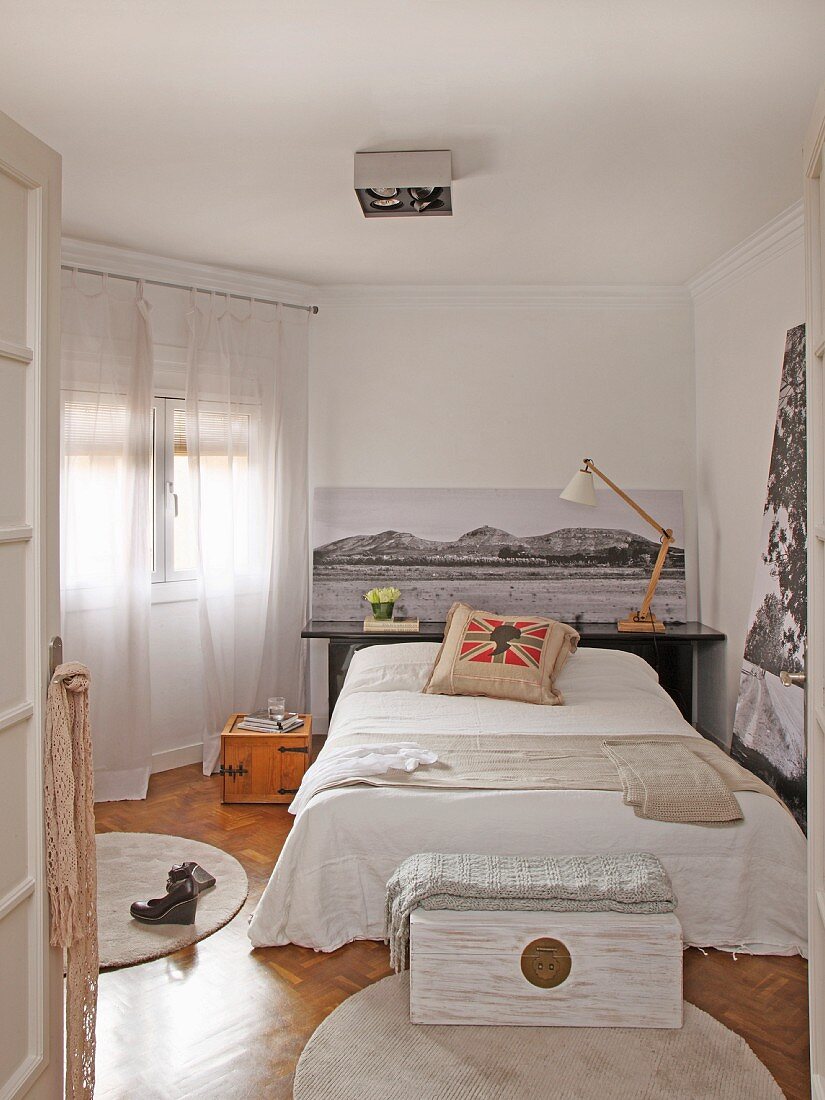 Schlafzimmer mit schwarz-weißen Fotoaufnahmen, Bett mit Dekokissen und Holztruhe auf rundem Teppich