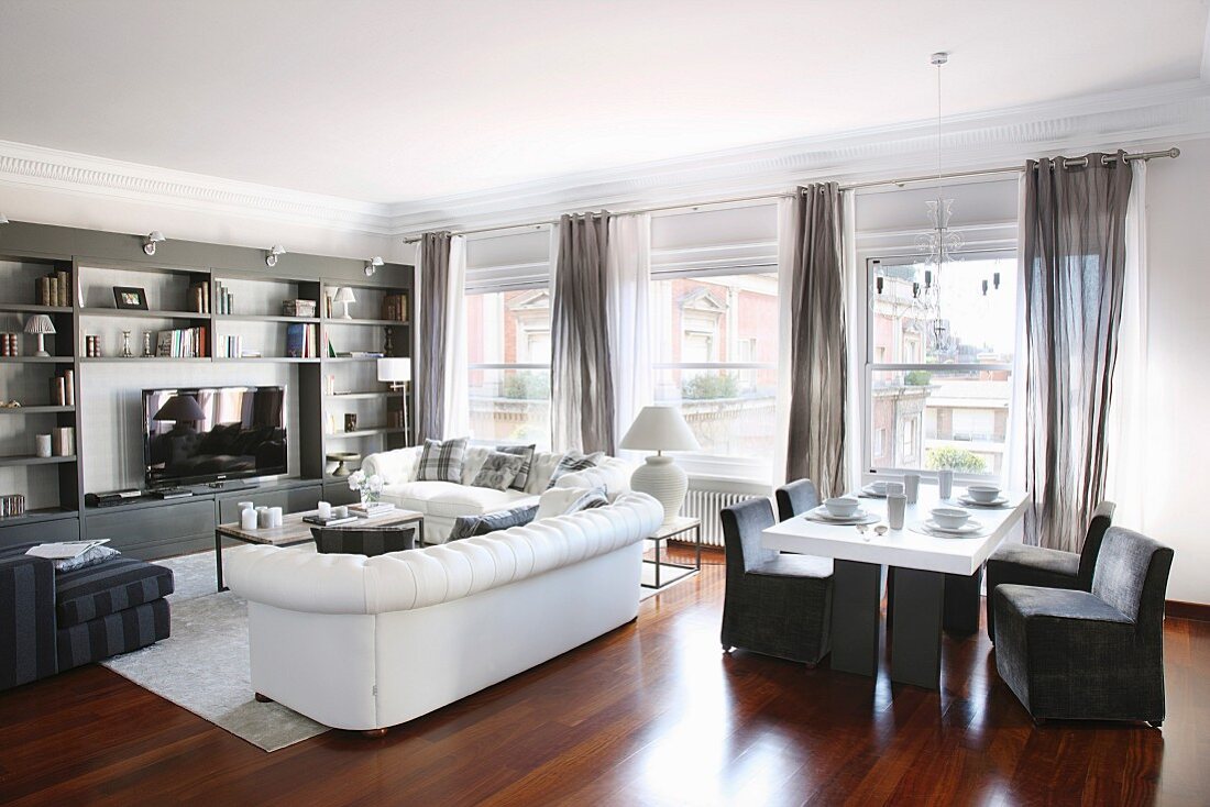 Eleganter Loungebereich mit weisser Sofagarnitur und Regalwand, Esstisch mit grauen Hussenstühlen