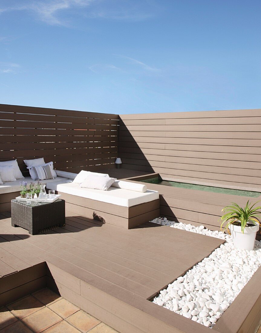 Elegant benches with white cushions and small bed of pebbles on sunny roof terrace