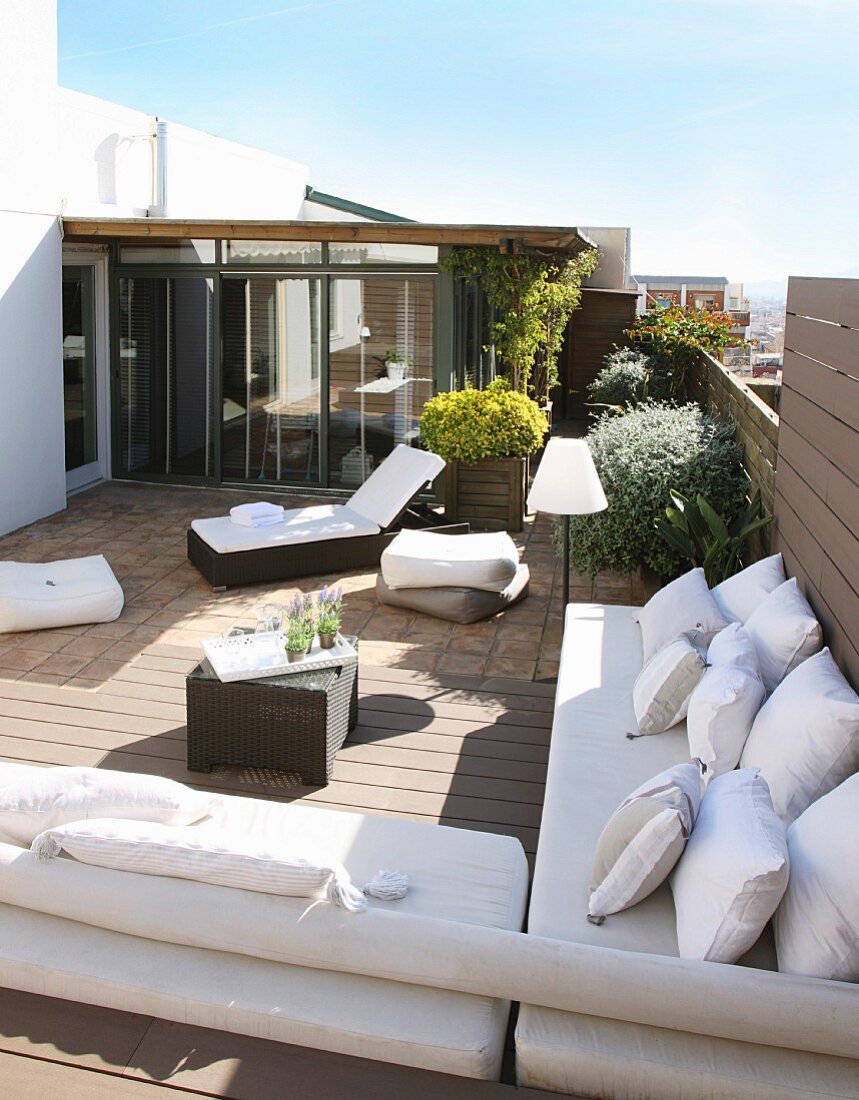 Elegante Liege und Sitzbänke mit weissen Auflagen und Kissen auf sonniger Dachterrasse